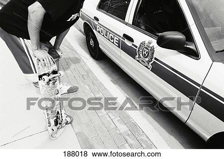 Stock Photo - Young man with skateboard leaning into police car. Fotosearch