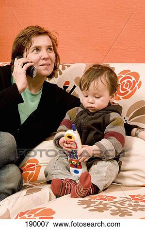 Stock Photo - Mother on the phone and baby boy with toy phone. Fotosearch