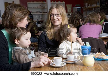 Stock Image - Two mother's in a cafe with children sitting on their laps. Fotosearch