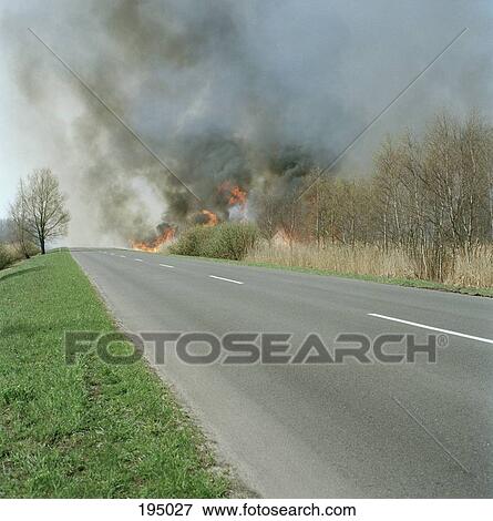 Stock Photo - A fire burning in a field on a roadside. Fotosearch