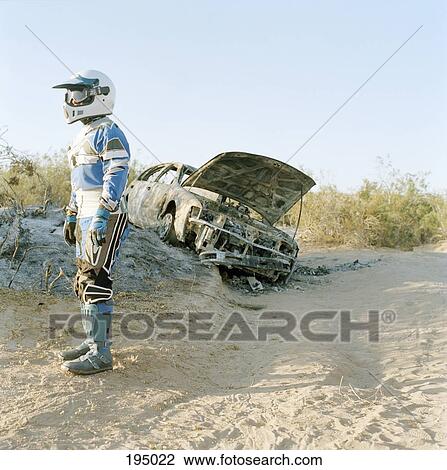 A motorcycle racer standing next to a burned-out car View Large Photo Image Stock Image - A motorcycle racer standing next to a burned-out car. Fotosearch