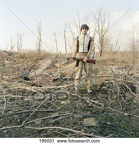 Stock Image - A woman standing in a field, holding a shotgun. Fotosearch