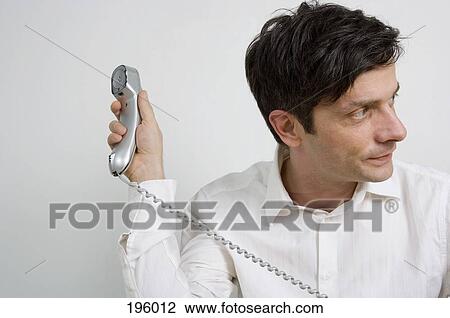 A man holding a telephone and looking away View Large Photo Image Stock Image - A man holding a telephone and looking away. Fotosearch