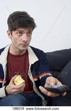 A man sitting on a couch with an apple and remote control View Large Photo Image Stock Photo - A man sitting on a couch with an apple and remote control. Fotosearch