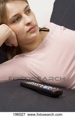 Stock Photo - a woman lying on a couch with remote control. Fotosearch
