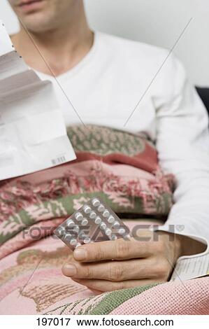 Stock Photo - A man holding a package of pills in bed. Fotosearch