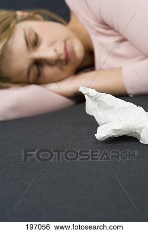 Stock Photograph - A woman with a cold lying next to a tissue. Fotosearch