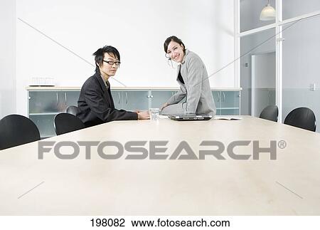 Stock Image - A man and woman sitting in a conference room, smiling. Fotosearch