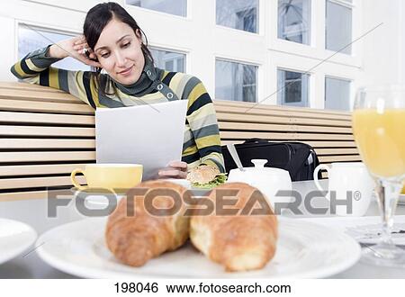 Stock Photograph - A woman reading paperwork while having breakfast. Fotosearch