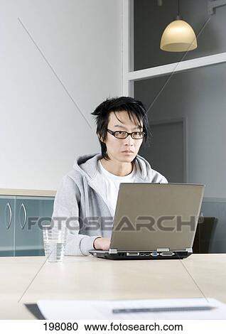 An Asian man working on a laptop in a conference room View Large Photo Image Stock Image - An Asian man working on a laptop in a conference room. Fotosearch