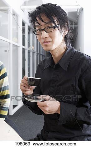 An Asian smiling while drinking coffee View Large Photo Image Stock Photo - An Asian smiling while drinking coffee. Fotosearch