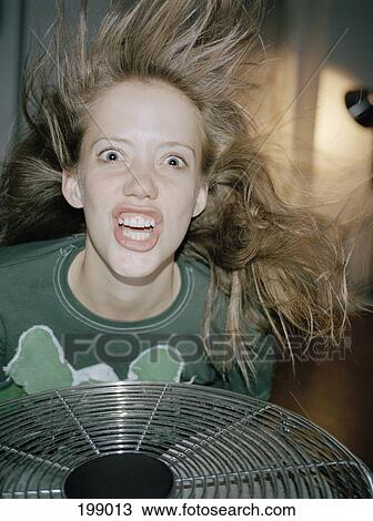 Stock Image - A woman making a crazy face above a fan. Fotosearch