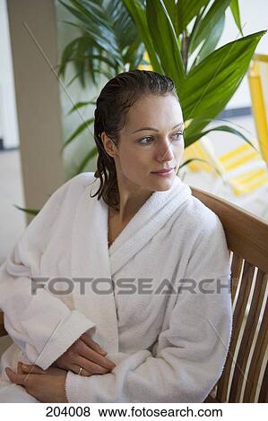 Stock Photo - Young woman sitting in bathrobe on wooden chair. Fotosearch