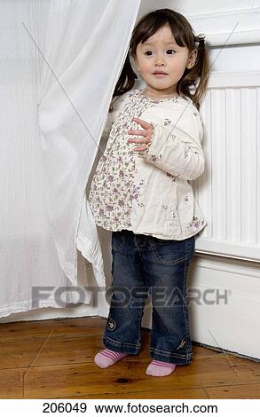 Stock Photo - A little girl standing next to a curtain. Fotosearch
