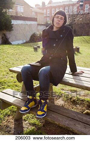 Stock Image - Mid adult woman sitting on picnic table in park. Fotosearch