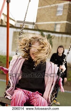 Picture - Young girl on swing with mother standing behind. Fotosearch