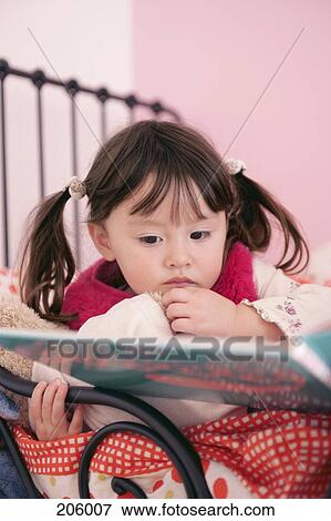 Young girl reclining on bed and looking at book View Large Photo Image Stock Photo - Young girl reclining on bed and looking at book. Fotosearch