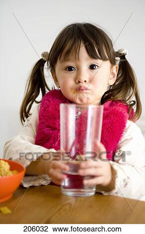 Young girl with pigtails sitting at table and holding glass of water View Large Photo Image Stock Image - Young girl with pigtails sitting at table and holding glass of water. Fotosearch