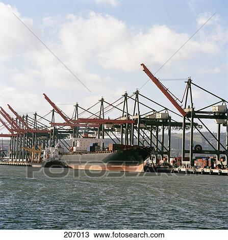 Stock Image - Cargo ship under red cranes on commercial dock. Fotosearch