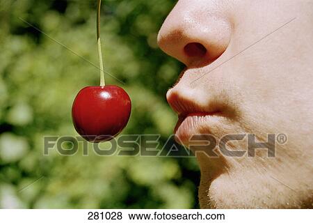 Young man holding a cherry near his mouth View Large Photo Image Stock Photo - Young man holding a cherry near his mouth. Fotosearch