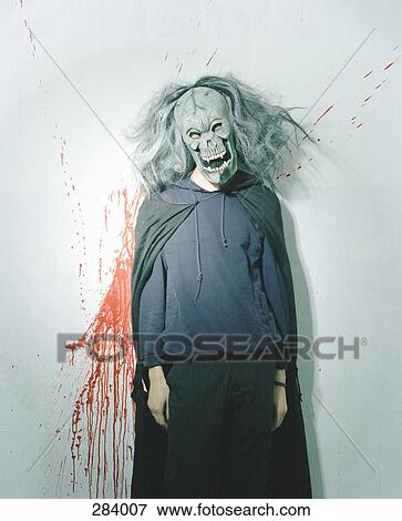 Stock Photo - Person dressed up in spooky mask and wig in front of blood splattered wall. Fotosearch