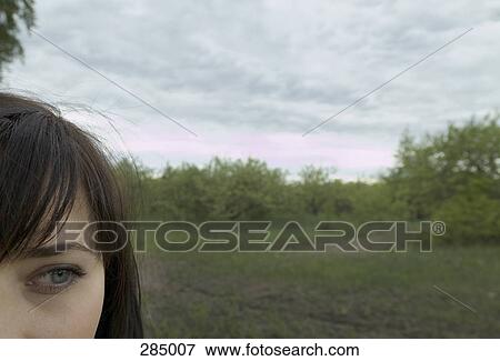 Stock Photo - Young woman standing in field with dramatic sky above. Fotosearch