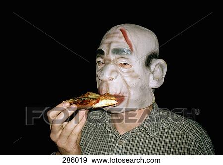 Stock Photo - Man wearing rubber monster mask and eating pizza. Fotosearch