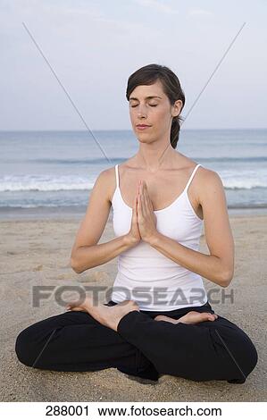 Stock Image - Woman sitting on beach in lotus position. Fotosearch