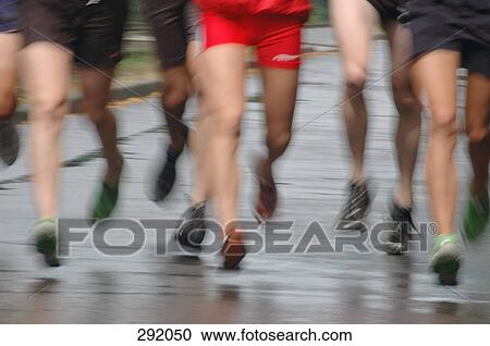 Stock Image - Group of men jogging on road together. Fotosearch