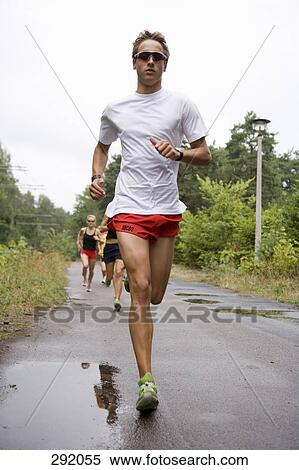 Stock Photography - Man running in front of other people jogging on road. Fotosearch