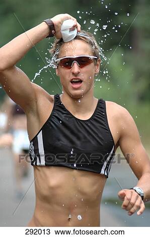Stock Image - Man running in sports race and pouring water over his head. Fotosearch