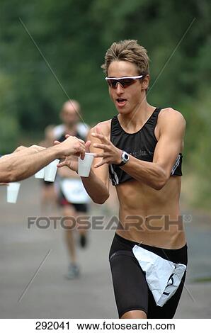 Stock Image - Man running in sports race and reaching for cup of water. Fotosearch