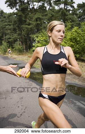 Picture - Woman running and reaching for wet sponge in sports race. Fotosearch