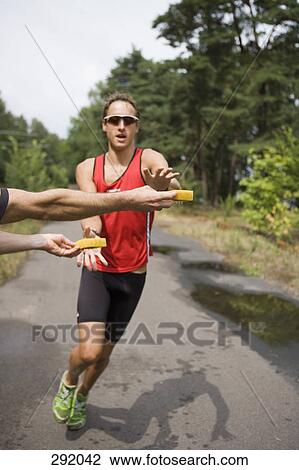 Stock Image - Young man running in sports race and reaching for wet sponges. Fotosearch