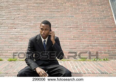 Businessman sitting on bench using mobile phone View Large Photo Image Stock Photograph - Businessman sitting on bench using mobile phone. Fotosearch