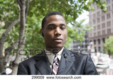 Businessman standing in financial district listening to headphones View Large Photo Image Stock Photo - Businessman standing in financial district listening to headphones. Fotosearch