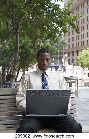 Young businessman sitting on park bench using laptop View Large Photo Image Stock Image - Young businessman sitting on park bench using laptop. Fotosearch