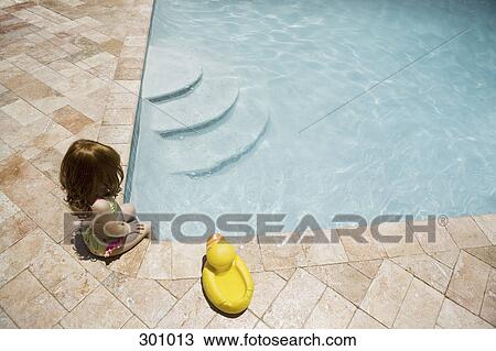 Stock Image - Girl sat on poolside with legs in pool. Fotosearch