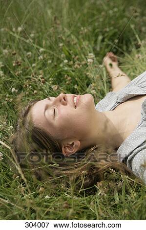 Stock Photo - Close-up of young woman lying in grass with eyes closed. Fotosearch