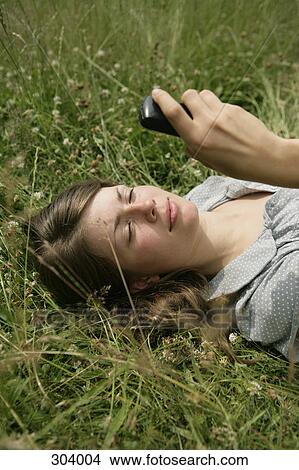 Picture - young woman lying in grass with mobile phone. Fotosearch