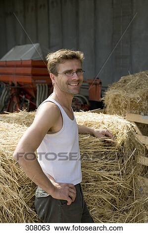 Farm worker resting next to bale of hay and smiling View Large Photo Image Stock Image - Farm worker resting next to bale of hay and smiling. Fotosearch