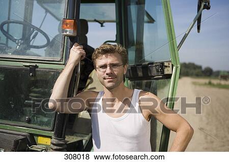 Farm worker standing next to tractor in field View Large Photo Image Stock Photo - Farm worker standing next to tractor in field. Fotosearch