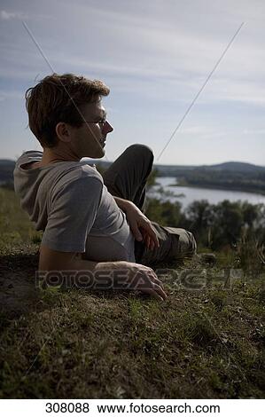 Stock Photo - Man relaxing on grass and looking at view. Fotosearch