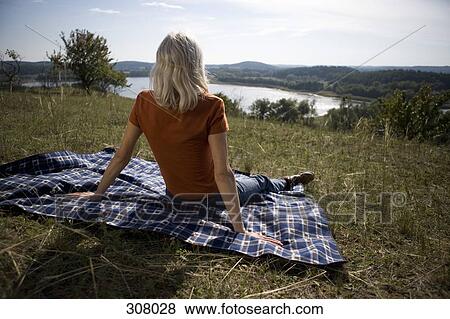 Stock Photo - Woman sitting on hill and looking at view. Fotosearch