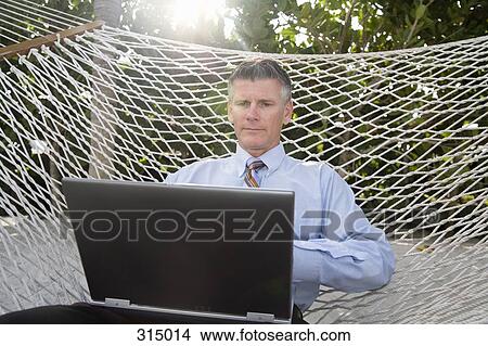 Man sitting in hammock and working on laptop View Large Photo Image Picture - Man sitting in hammock and working on laptop. Fotosearch