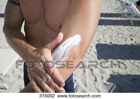 Man standing on beach and applying sun cream to arm View Large Photo Image Stock Image - Man standing on beach and applying sun cream to arm. Fotosearch