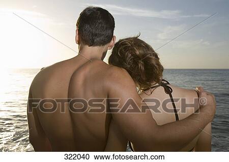 Stock Image - Couple embracing on beach at sunset. Fotosearch