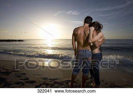 Stock Image - Couple embracing on beach at sunset. Fotosearch