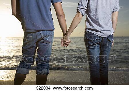 Man and woman holding hands on beach and looking at sunset together View Large Photo Image Picture - Man and woman holding hands on beach and looking at sunset together. Fotosearch