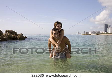 Stock Photography - Man giving woman a piggyback in sea. Fotosearch